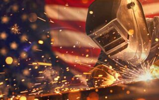 Welder working with sparks flying in front of an American flag, symbolizing strength and precision in U.S. manufacturing.