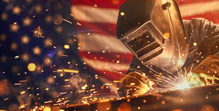 Welder working with sparks flying in front of an American flag, symbolizing strength and precision in U.S. manufacturing.